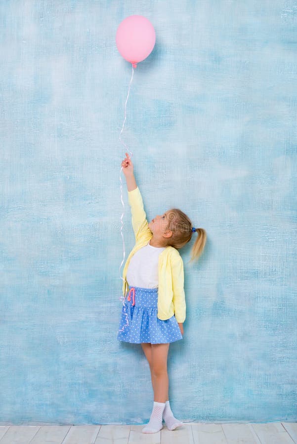 In voller Länge Nettes kleines Mädchen, das einen rosa Ballon auf einem blauen Hintergrund hält