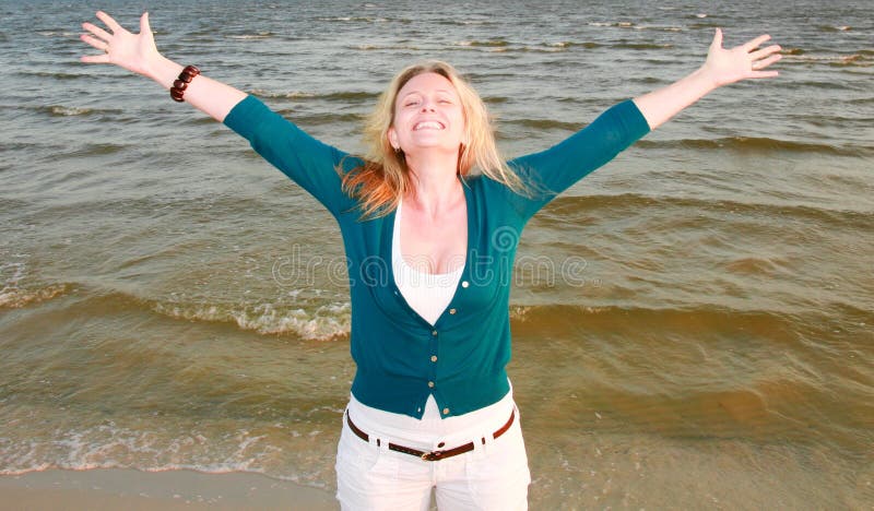 A beautiful woman smiling with arms open with water in the background. A beautiful woman smiling with arms open with water in the background.