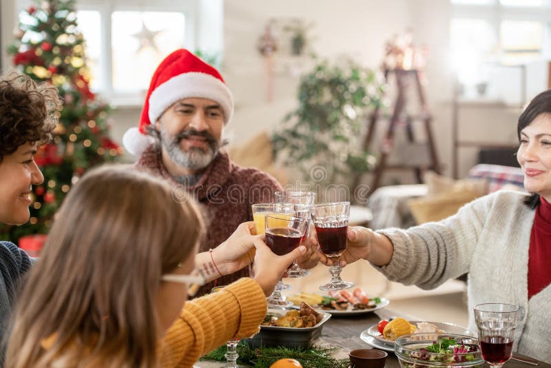 Mature couple, young woman and cute girl clinking with flutes of homemade drinks over festive table served with traditional xmas food. Mature couple, young woman and cute girl clinking with flutes of homemade drinks over festive table served with traditional xmas food