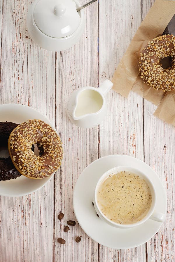 Voor een licht houten achtergrondochtendontbijt, een Kop van koffie met melk en donuts met chocolade Verticale, hoogste mening royalty-vrije stock foto's Voor een licht houten achtergrondochtendontbijt, een Kop van koffie met melk en donuts met chocolade Verticale, hoogste mening royalty-vrije stock foto's