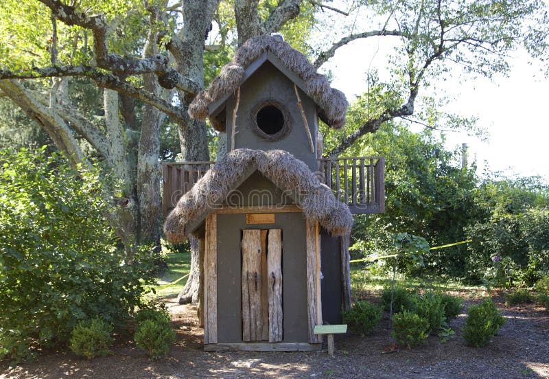 A fancifully crafted tree house sits in a forest courtyard. A fancifully crafted tree house sits in a forest courtyard.