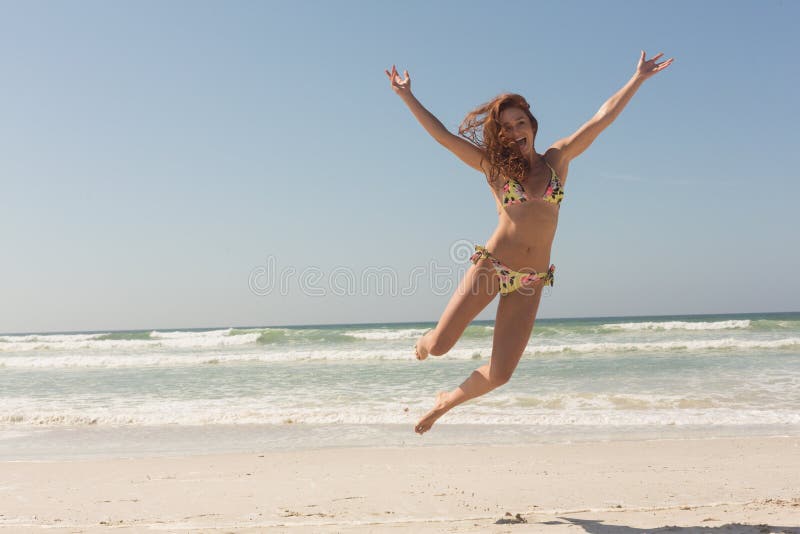 Vooraanzicht van mooie jonge Kaukasische vrouw die in bikini op het strand springen stock foto Vooraanzicht van mooie jonge Kaukasische vrouw die in bikini op het strand springen stock foto
