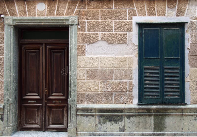 Voorgevel van een oud Spaans huis met donkere bruine houten deur in een steenkader en zwarte gesloten blinden met oude afbrokkele royalty-vrije stock afbeelding Voorgevel van een oud Spaans huis met donkere bruine houten deur in een steenkader en zwarte gesloten blinden met oude afbrokkele royalty-vrije stock afbeelding