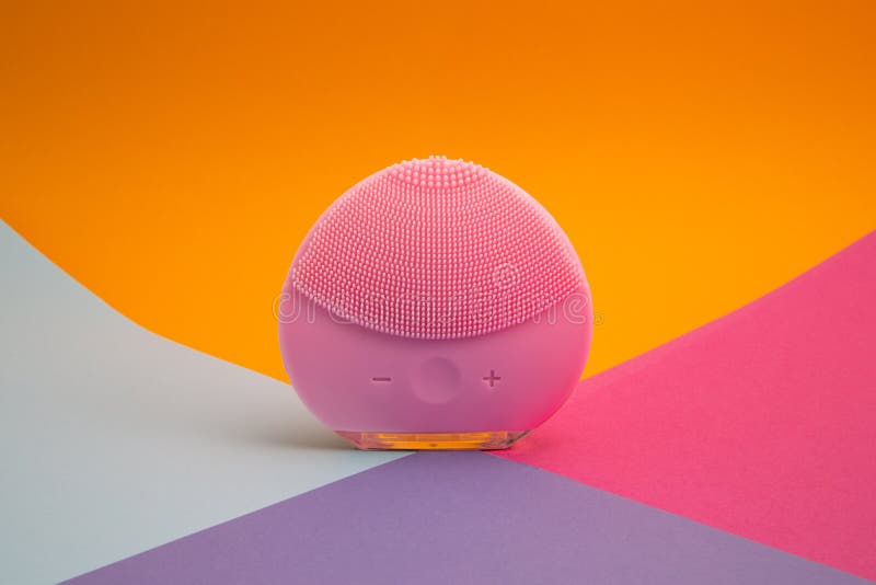 Front side of a mini magenta silicone vibrating facial cleansing brush on colorful background, close up with copy space. Front side of a mini magenta silicone vibrating facial cleansing brush on colorful background, close up with copy space