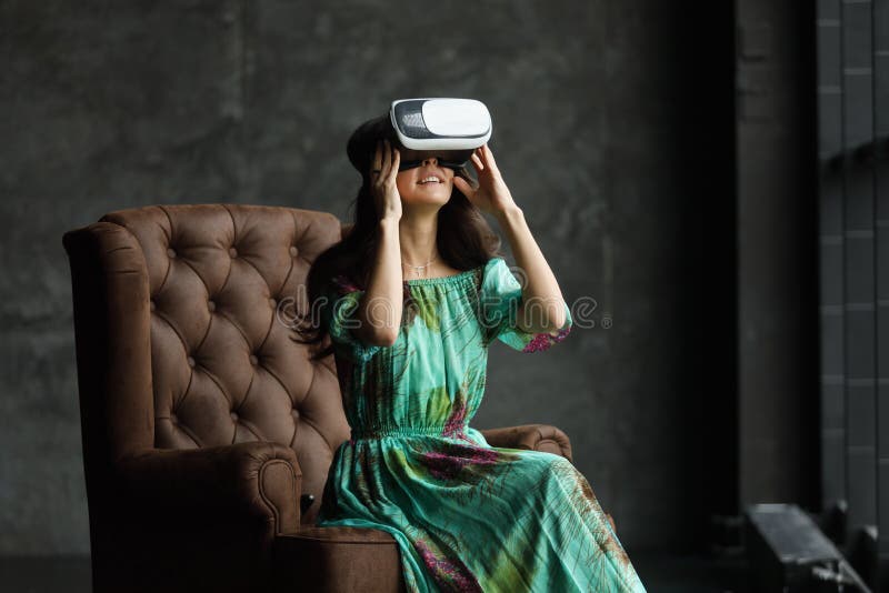 The VR headset design is generic and no logos, Woman with glasses of virtual reality, Sits in a chair, against a dark background. royalty free stock image The VR headset design is generic and no logos, Woman with glasses of virtual reality, Sits in a chair, against a dark background. royalty free stock image