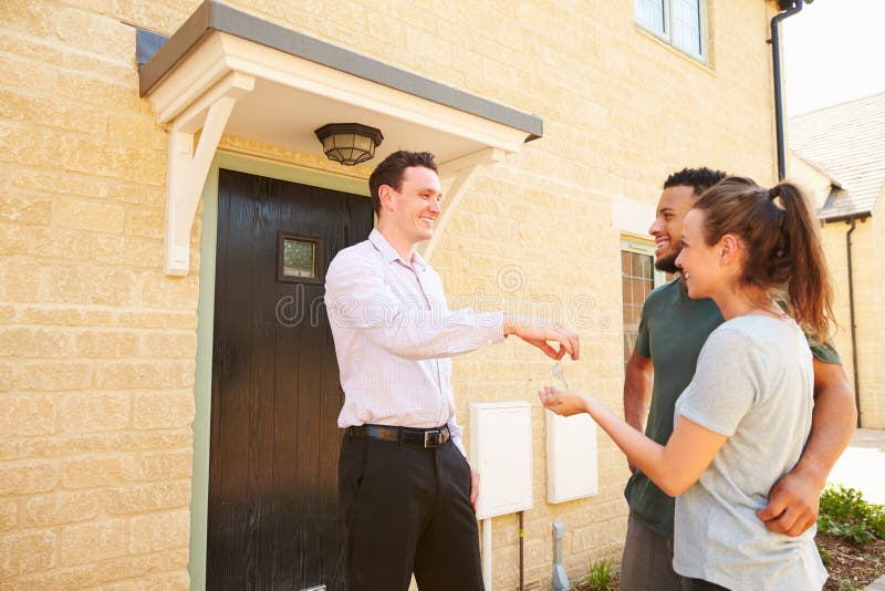 Vrai agent immobilier donnant des clés de maison à de nouveaux propriétaires images libres de droits Vrai agent immobilier donnant des clés de maison à de nouveaux propriétaires images libres de droits