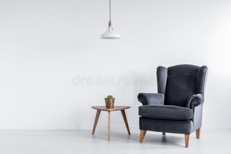 Vraie photo de fauteuil gris-foncé se tenant à côté de la table d'extrémité en bois avec le cactus dans l'intérieur lumineux de c image libre de droits Vraie photo de fauteuil gris-foncé se tenant à côté de la table d'extrémité en bois avec le cactus dans l'intérieur lumineux de c image libre de droits