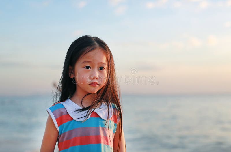 Vreedzaam weinig kindmeisje die zich op strand bij zonsonderganglicht bevinden met het kijken camera stock afbeelding Vreedzaam weinig kindmeisje die zich op strand bij zonsonderganglicht bevinden met het kijken camera stock afbeelding