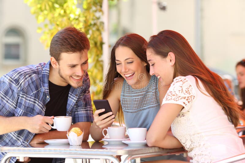 Vrienden die op media in een slimme telefoon in een koffiewinkel letten stock afbeeldingen Vrienden die op media in een slimme telefoon in een koffiewinkel letten stock afbeeldingen