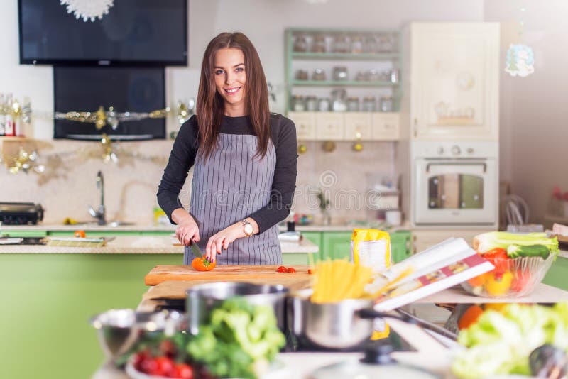 Vrij jonge Kaukasische vrouw die pizza maken door receptenboek, die groenten op scherpe raad in haar vlakte hakken royalty-vrije stock fotografie Vrij jonge Kaukasische vrouw die pizza maken door receptenboek, die groenten op scherpe raad in haar vlakte hakken royalty-vrije stock fotografie