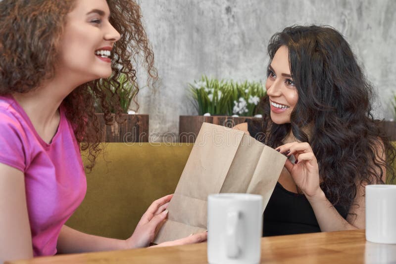 Vrij krullende vrouw die aan vrouwelijke vriend in koffie huidig maakt stock afbeeldingen Vrij krullende vrouw die aan vrouwelijke vriend in koffie huidig maakt stock afbeeldingen