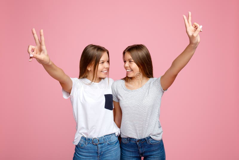 Vrij twee jonge tweelingzusters met mooie glimlach met handen die vredesgebaar over roze achtergrond tonen stock afbeelding Vrij twee jonge tweelingzusters met mooie glimlach met handen die vredesgebaar over roze achtergrond tonen stock afbeelding