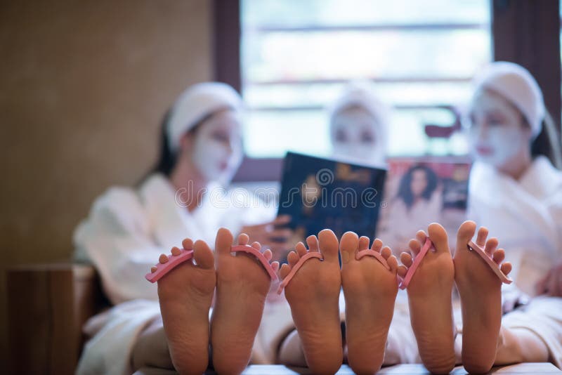 Bachelorette party in spa, girls with face mask reading magazine, pedicure concept, foots with seperator in focus. Bachelorette party in spa, girls with face mask reading magazine, pedicure concept, foots with seperator in focus