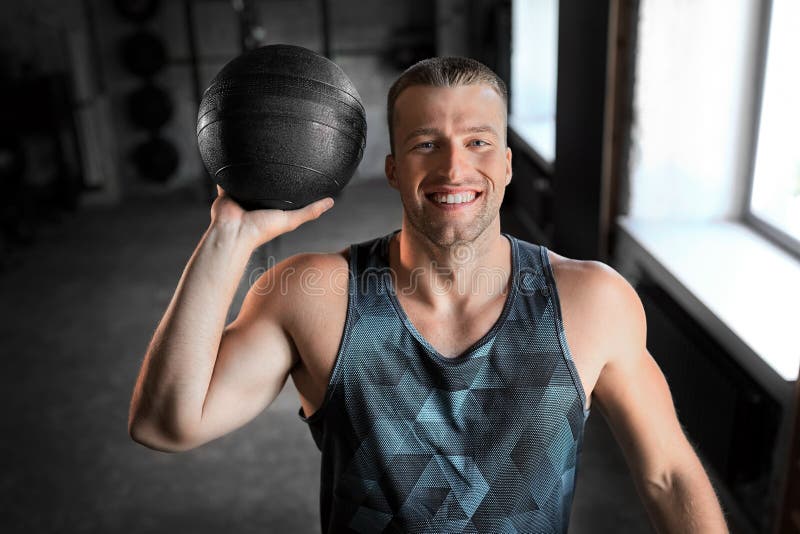 Vrolijk glimlachen van jonge man met medicijnbal in gym