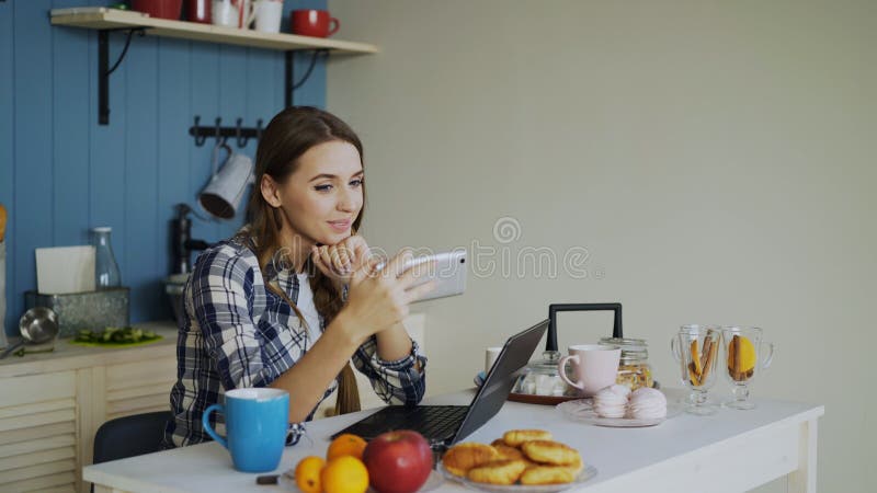 Vrolijk het glimlachen woamn het spreken online videopraatje die smartphone in de keuken thuis gebruiken stock afbeelding Vrolijk het glimlachen woamn het spreken online videopraatje die smartphone in de keuken thuis gebruiken stock afbeelding