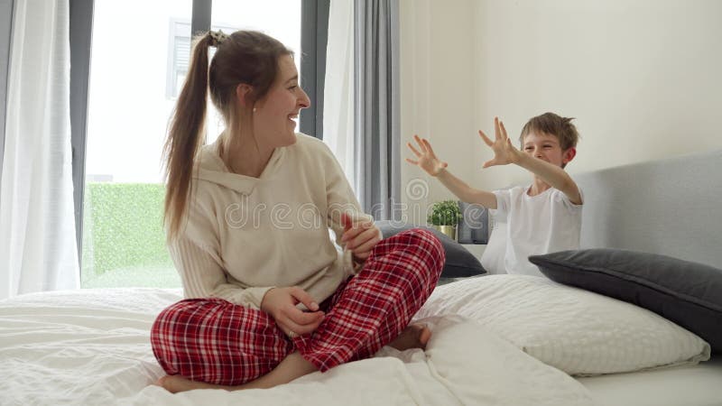 Vrolijk lachende jongen bang en speelt met moeder die een pyjama op bed draagt. begrip gelukkige ouders met kinderen.