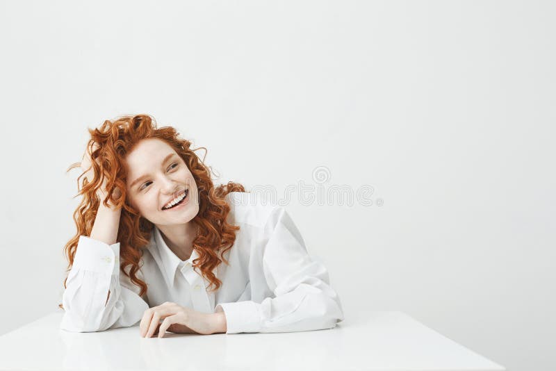 Vrolijk vrij jong meisje met foxy haar het glimlachen het lachen zitting bij lijst over witte achtergrond stock afbeeldingen Vrolijk vrij jong meisje met foxy haar het glimlachen het lachen zitting bij lijst over witte achtergrond stock afbeeldingen