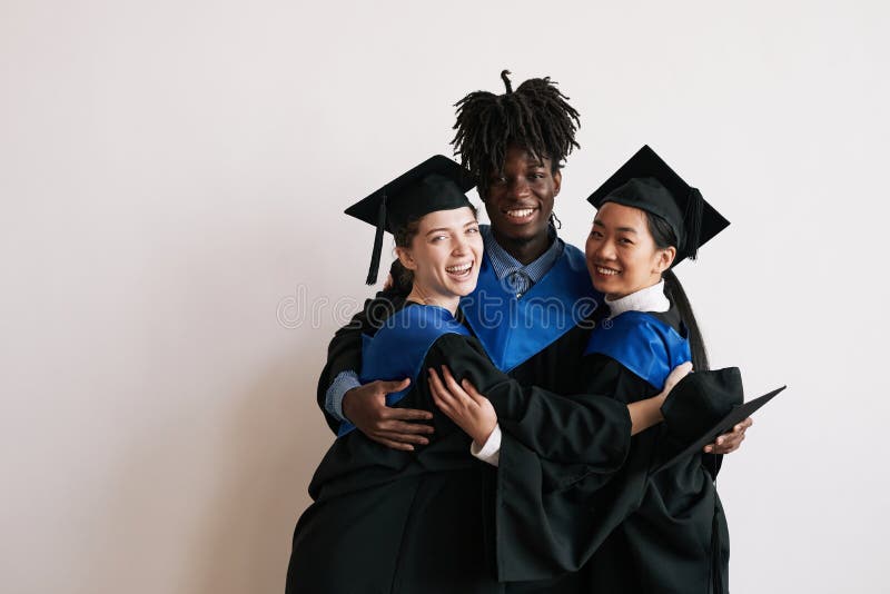 Waist up portrait of three happy college graduates wearing robes and embracing while smiling at camera, copy space. Waist up portrait of three happy college graduates wearing robes and embracing while smiling at camera, copy space