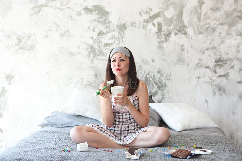Vrolijke droevige jonge craing vrouw die snoepjes in haar slaapkamer eten stock foto Vrolijke droevige jonge craing vrouw die snoepjes in haar slaapkamer eten stock foto