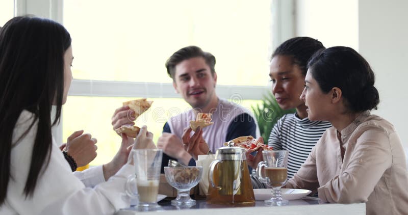 Vrolijke en gevarieerde jonge vrienden die pizza eten in café