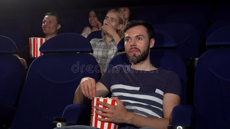 Vrolijke jonge mens die duimen tonen terwijl lettende op films bij de bioskoop