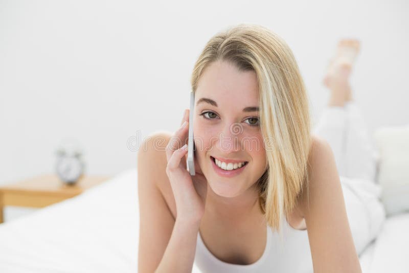 Vrolijke jonge vrouw die bij camera glimlachen terwijl het telefoneren met haar smartphone stock fotografie Vrolijke jonge vrouw die bij camera glimlachen terwijl het telefoneren met haar smartphone stock fotografie
