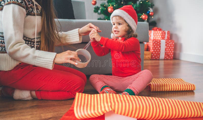 Vrolijke Kerstmis en Gelukkig Nieuwjaar Het meisje en de jonge vrouw zitten op vloer Het kind bereikt en raakt band De vrouw houd royalty-vrije stock afbeelding Vrolijke Kerstmis en Gelukkig Nieuwjaar Het meisje en de jonge vrouw zitten op vloer Het kind bereikt en raakt band De vrouw houd royalty-vrije stock afbeelding