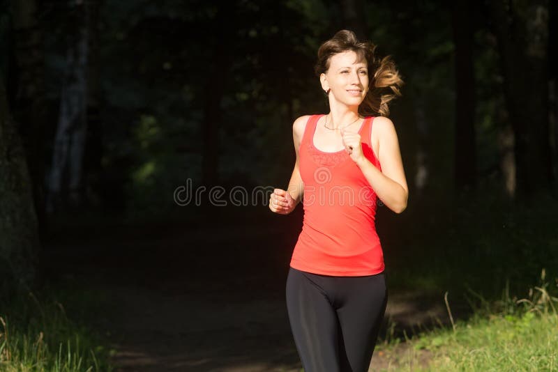 Vrolijke meisjesjogging bij ochtend in de zomerpark De glimlachende jonge Kaukasische vrouw kleedde zich uit in sportwear looppas royalty-vrije stock afbeelding Vrolijke meisjesjogging bij ochtend in de zomerpark De glimlachende jonge Kaukasische vrouw kleedde zich uit in sportwear looppas royalty-vrije stock afbeelding