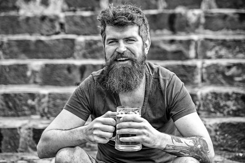 Vrolijke mens die met bier in zijn handen op steentrap binnen zitten de stad in Glimlachende jonge mens met modieuze baard stock foto Vrolijke mens die met bier in zijn handen op steentrap binnen zitten de stad in Glimlachende jonge mens met modieuze baard stock foto