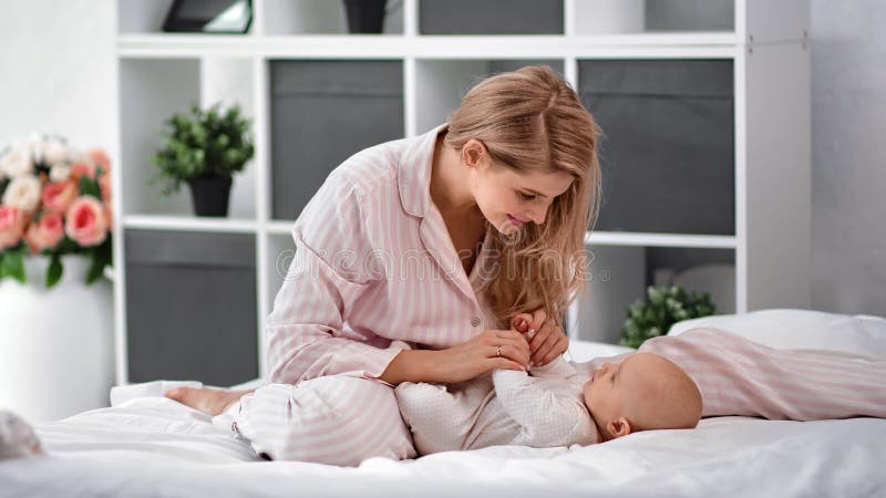 Vrolijke moeder die speelt met schattige baby die op bed zit in een luie witte kamer. met rode camera in 4.000