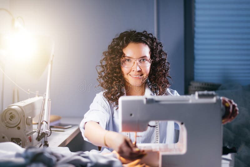 Vrolijke naaister stemmende naaimachine voor het werk bij aangestoken studio stock foto's Vrolijke naaister stemmende naaimachine voor het werk bij aangestoken studio stock foto's