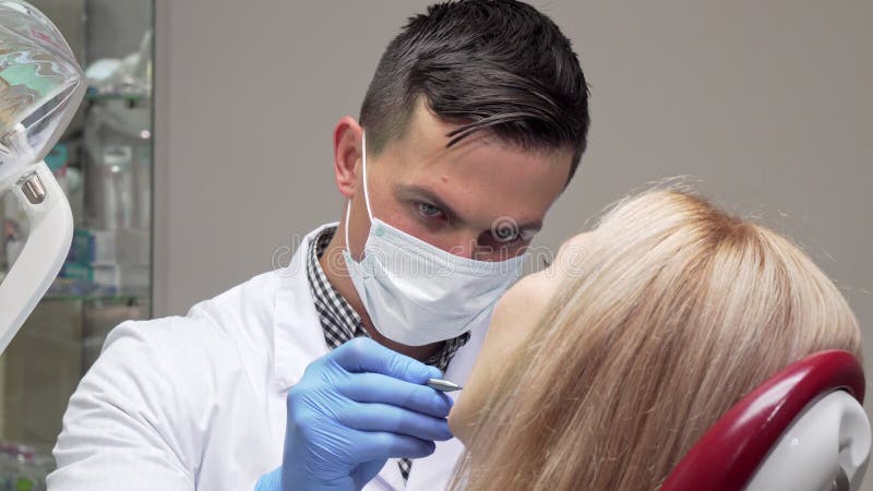 Vrolijke tandarts die in medisch masker terwijl het onderzoeken van tanden van een patiënt lachen