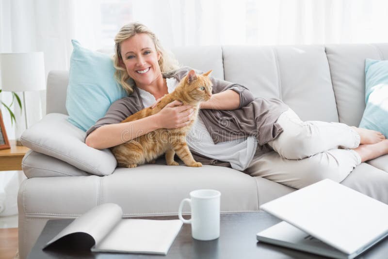 Vrolijke vrouw die op bank liggen die een gemberkat knuffelen stock fotografie Vrolijke vrouw die op bank liggen die een gemberkat knuffelen stock fotografie