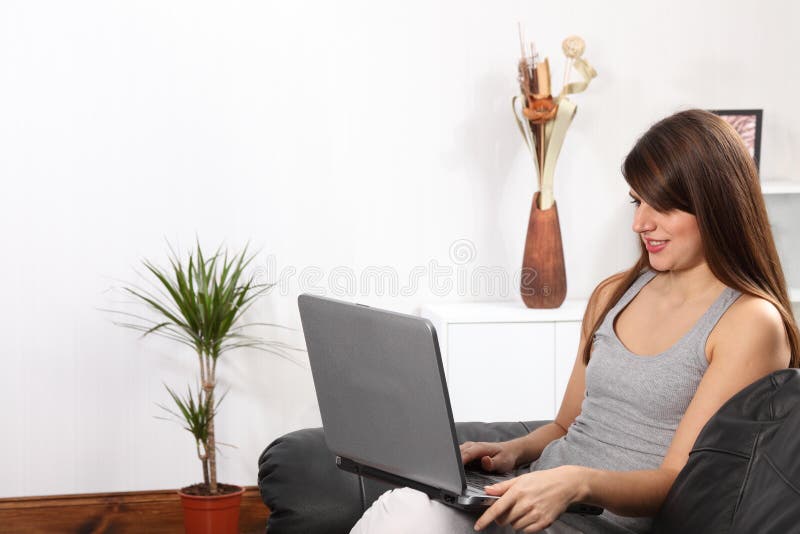 Vrolijke vrouw thuis op bank die laptop met behulp van stock afbeelding Vrolijke vrouw thuis op bank die laptop met behulp van stock afbeelding