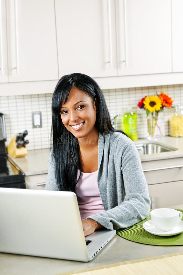 Smiling black woman using computer in modern kitchen interior. Smiling black woman using computer in modern kitchen interior