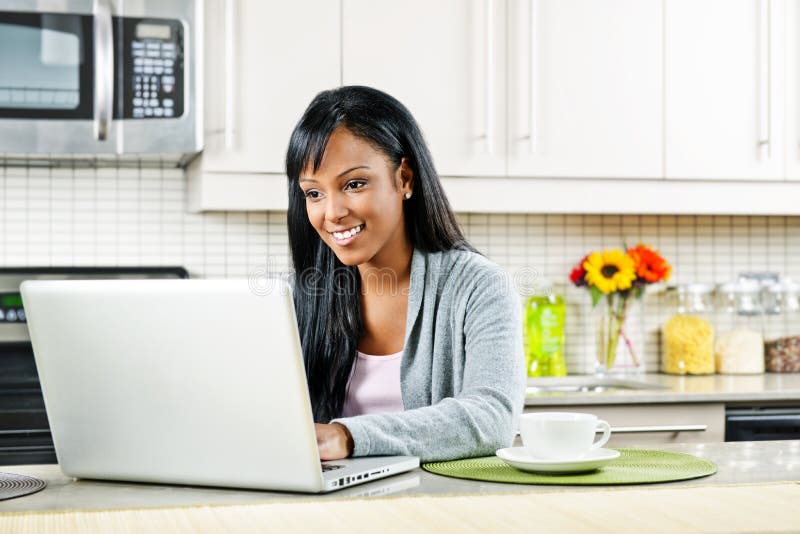 Smiling black woman using computer in modern kitchen interior. Smiling black woman using computer in modern kitchen interior