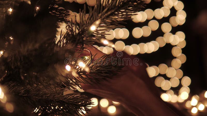 Vrouw die de lichten op een Kerstboom met de achtergrond van bokehlichten verfraaien