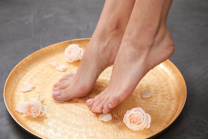 Vrouw die haar voeten in plaat met water en rozen op grijze achtergrond, close-up doorweken