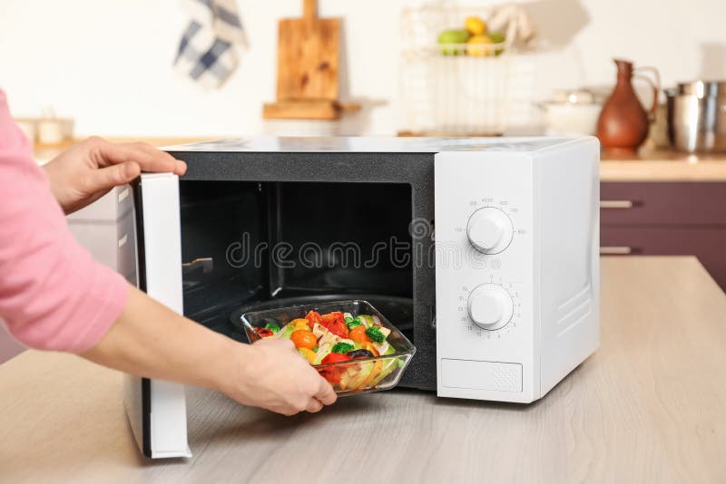 Vrouw die kom met groenten in magnetron zetten stock afbeelding Vrouw die kom met groenten in magnetron zetten stock afbeelding