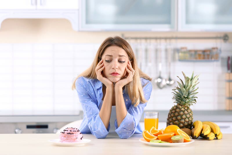 Vrouw die tussen dessert en vruchten bij lijst in keuken kiezen royalty-vrije stock afbeelding Vrouw die tussen dessert en vruchten bij lijst in keuken kiezen royalty-vrije stock afbeelding