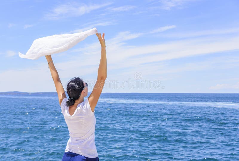Vrouw die van het zeebries genieten die een zijdezakdoek houden die door de wind tegen het overzees wordt gegolft royalty-vrije stock fotografie Vrouw die van het zeebries genieten die een zijdezakdoek houden die door de wind tegen het overzees wordt gegolft royalty-vrije stock fotografie