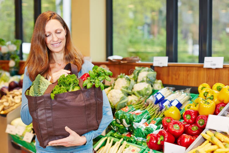 Vrouw die verse groenten in natuurvoedingopslag kopen