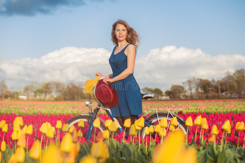 Vrouw die zich met haar fiets op tulpengebieden bevinden royalty-vrije stock afbeeldingen Vrouw die zich met haar fiets op tulpengebieden bevinden royalty-vrije stock afbeeldingen