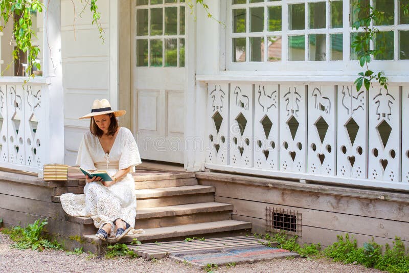 Vrouw in een witte kleding en een strohoed die een boek op por lezen stock foto Vrouw in een witte kleding en een strohoed die een boek op por lezen stock foto