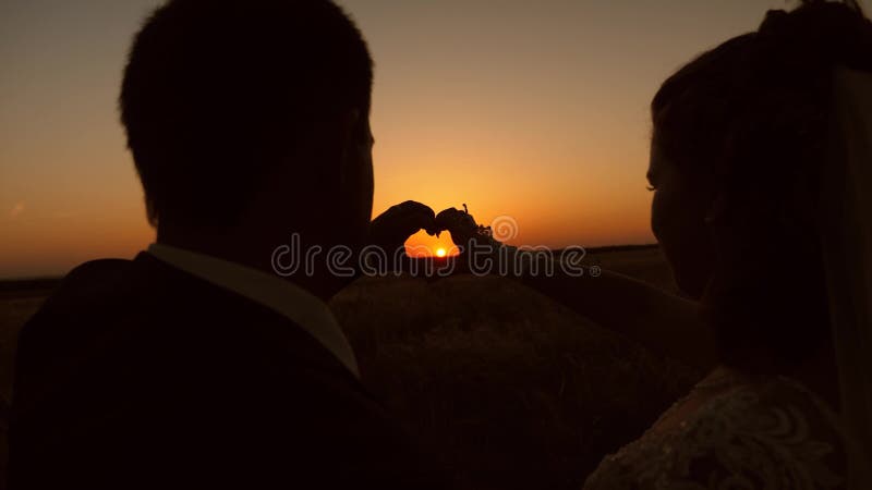 Vrouw en man die hartsignalen afgeven met handen voor een mooie zonsondergang aan de horizon de zon ligt in de handen teamwork