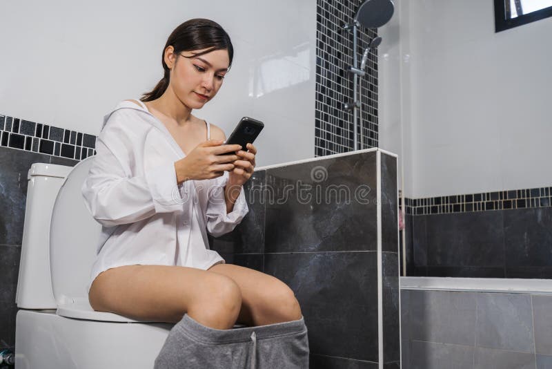 Vrouw gebruikend mobiele telefoon en zittend op toilet stock afbeeldingen Vrouw gebruikend mobiele telefoon en zittend op toilet stock afbeeldingen