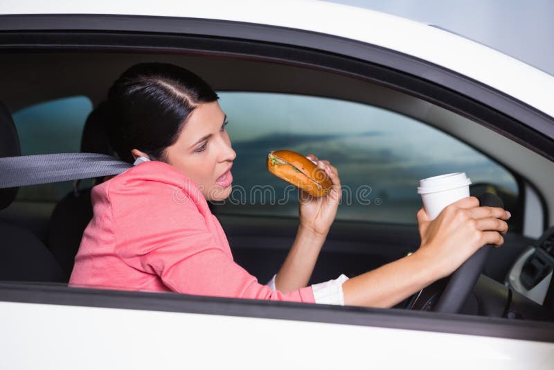 Woman drinking coffee and eating sandwich on phone in her car. Woman drinking coffee and eating sandwich on phone in her car