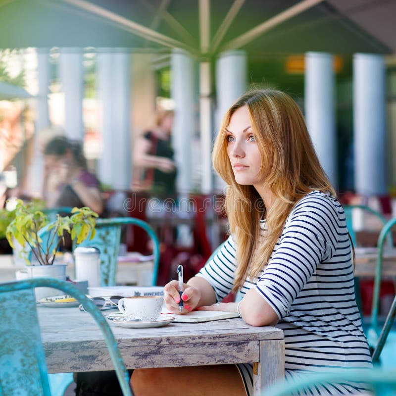 Young beautiful woman drinking coffee and writing diary, book or notes in an outdoor cafe in Berlin, Germany. Young beautiful woman drinking coffee and writing diary, book or notes in an outdoor cafe in Berlin, Germany.