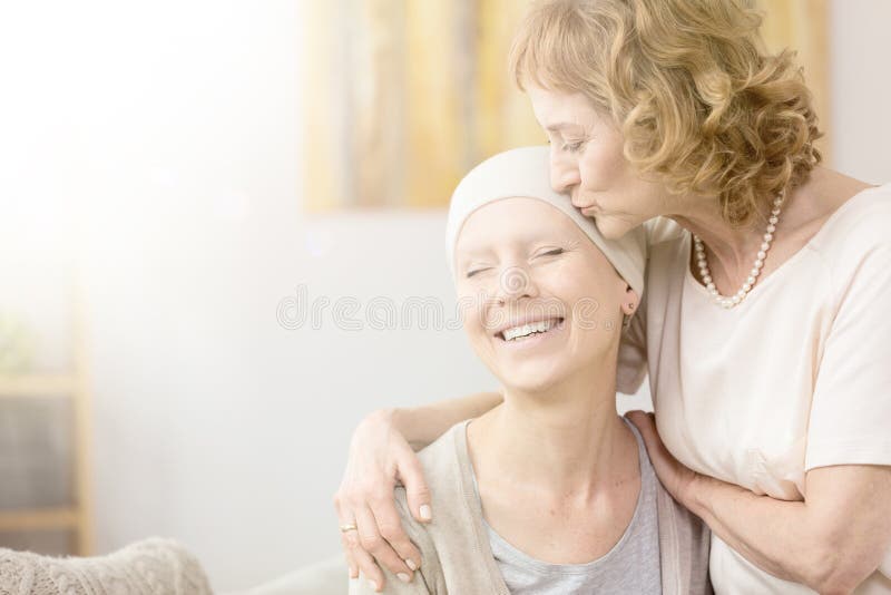 Elderly women kissing happy cancer survivor`s temple, comforting her friend. Elderly women kissing happy cancer survivor`s temple, comforting her friend