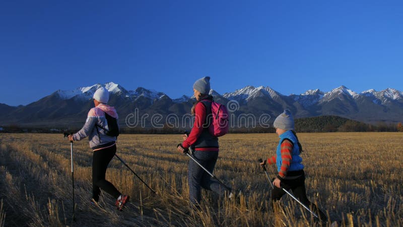Vrouw loopt noords in de natuur op de achtergrond van bergen in het veld Meisjes en kinderen gebruiken trekstokken en noordse